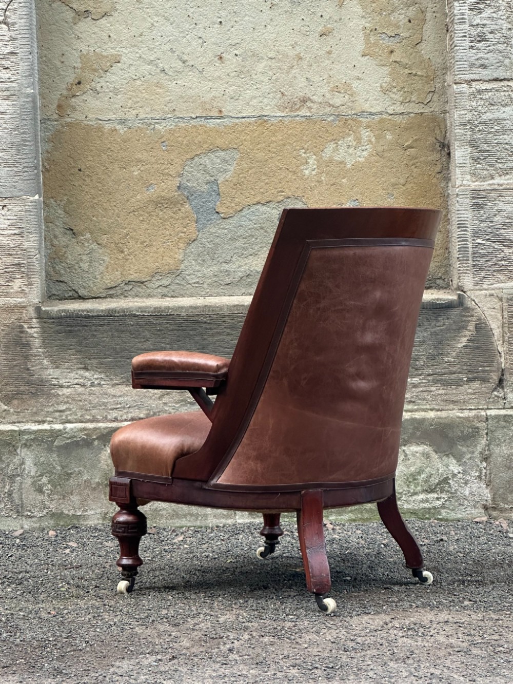 A pair of nineteenth-century Greek Revival mahogany armchairs upholstered in warm brown leather with turned front legs on castors and incised geometric detailing. View XII