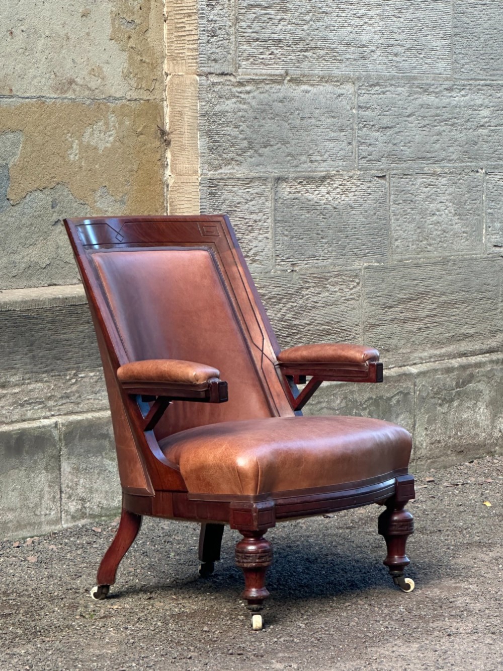 A pair of nineteenth-century Greek Revival mahogany armchairs upholstered in warm brown leather with turned front legs on castors and incised geometric detailing. View XIV