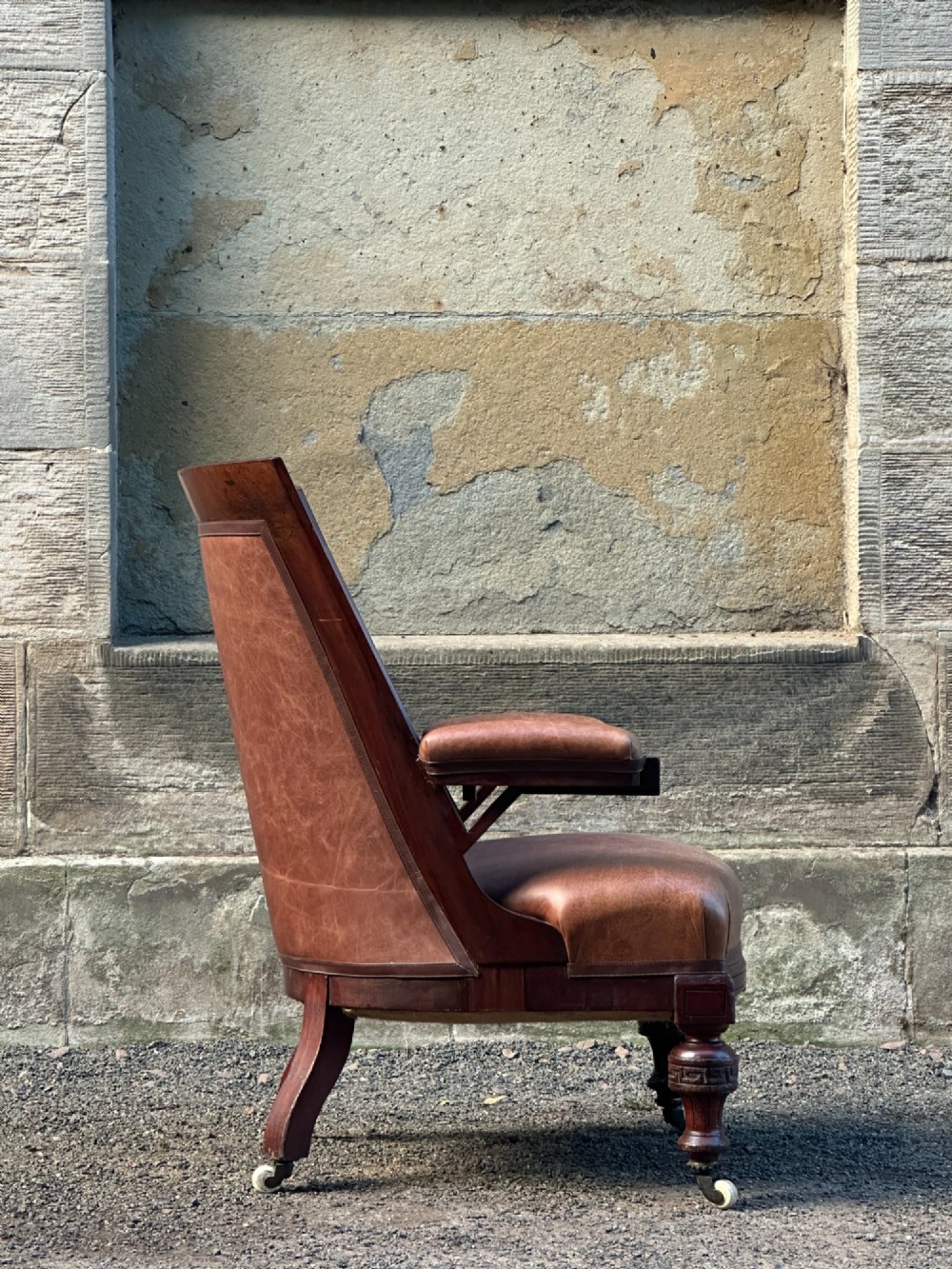 A pair of nineteenth-century Greek Revival mahogany armchairs upholstered in warm brown leather with turned front legs on castors and incised geometric detailing. View XV