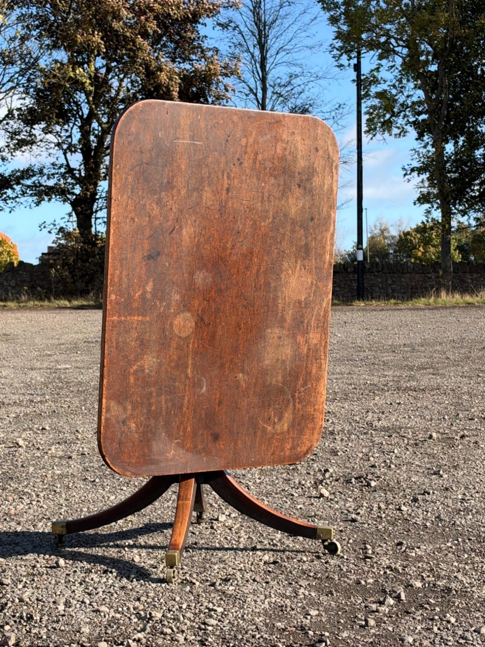 A late George III mahogany snap-top dining table featuring a rectangular surface resting on a turned pedestal column and four splayed legs with brass castors. View II
