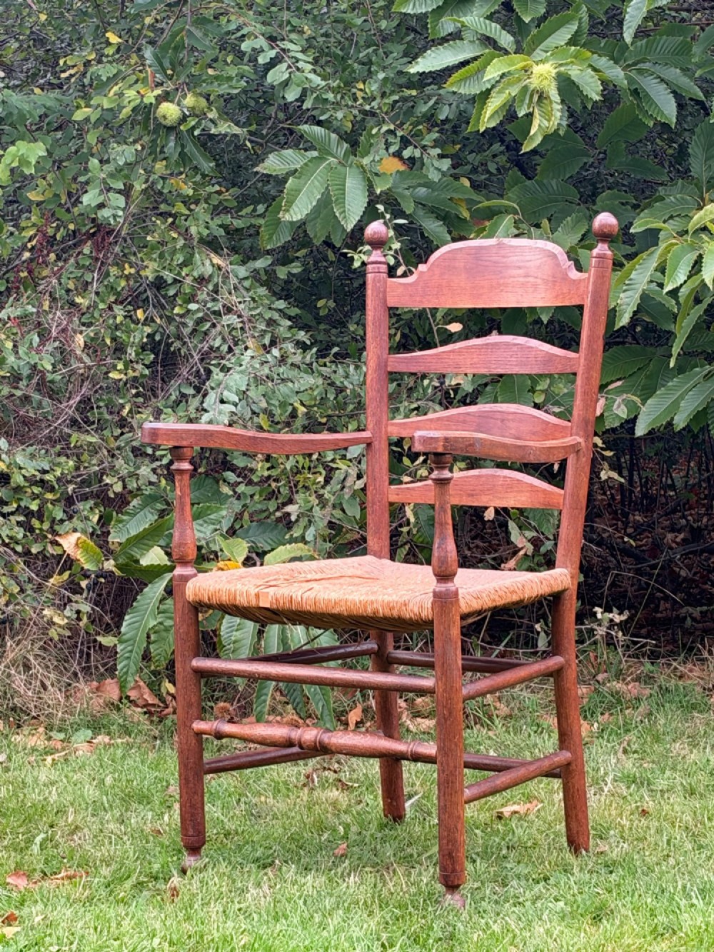 An early 20th-century Anglo-Indian armchair made of medium brown teak with a ladder back, turned front legs, shaped armrests, and a woven rush seat. View II