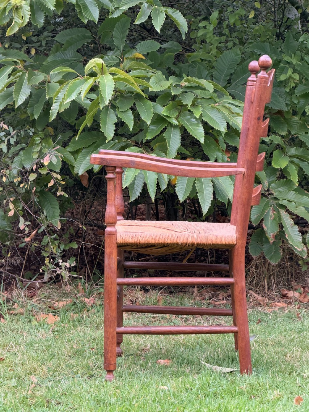 An early 20th-century Anglo-Indian armchair made of medium brown teak with a ladder back, turned front legs, shaped armrests, and a woven rush seat. View V