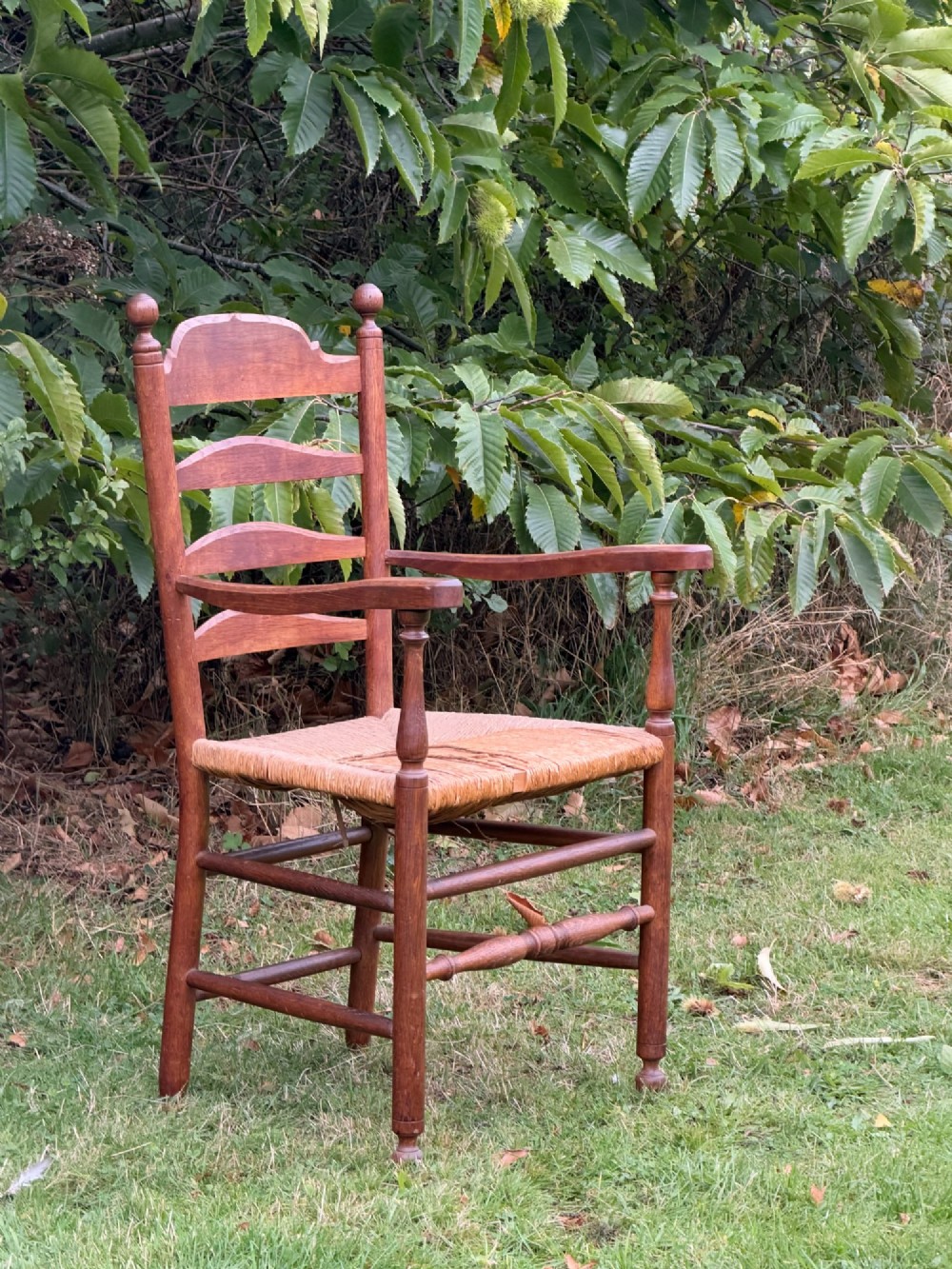 An early 20th-century Anglo-Indian armchair made of medium brown teak with a ladder back, turned front legs, shaped armrests, and a woven rush seat. View VIII