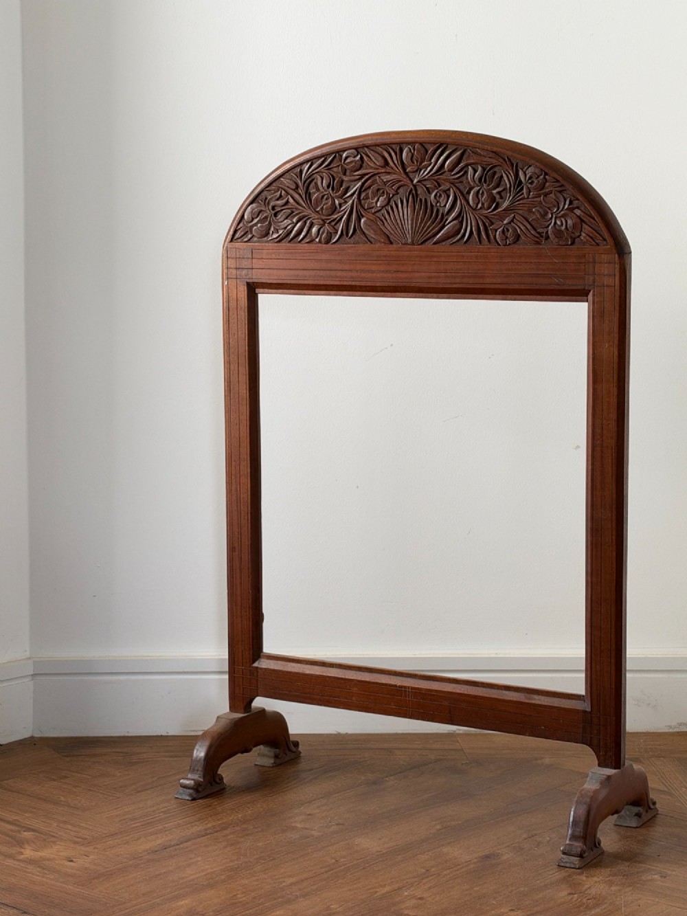 A freestanding Anglo-Indian carved walnut screen frame featuring an arched floral crest and splayed scrolled feet.