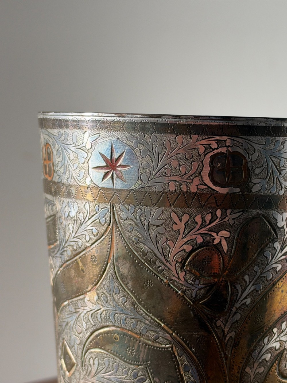 A tapered white metal beaker featuring detailed hand-engraved foliage motifs, star emblems, and a tarnished patina. View III