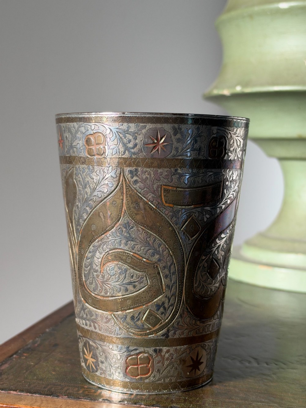 A tapered white metal beaker featuring detailed hand-engraved foliage motifs, star emblems, and a tarnished patina. View IV