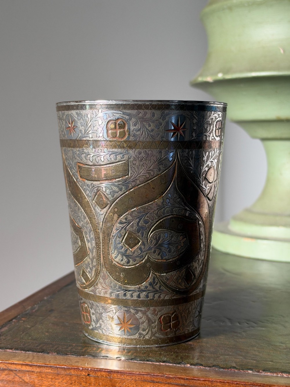 A tapered white metal beaker featuring detailed hand-engraved foliage motifs, star emblems, and a tarnished patina. View V
