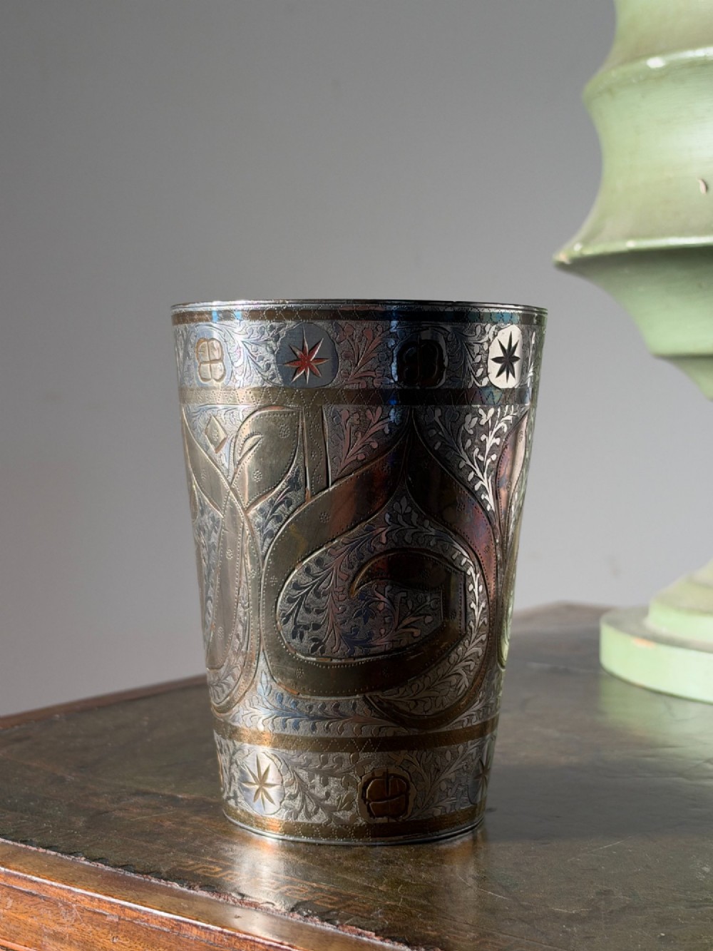 A tapered white metal beaker featuring detailed hand-engraved foliage motifs, star emblems, and a tarnished patina. View VI