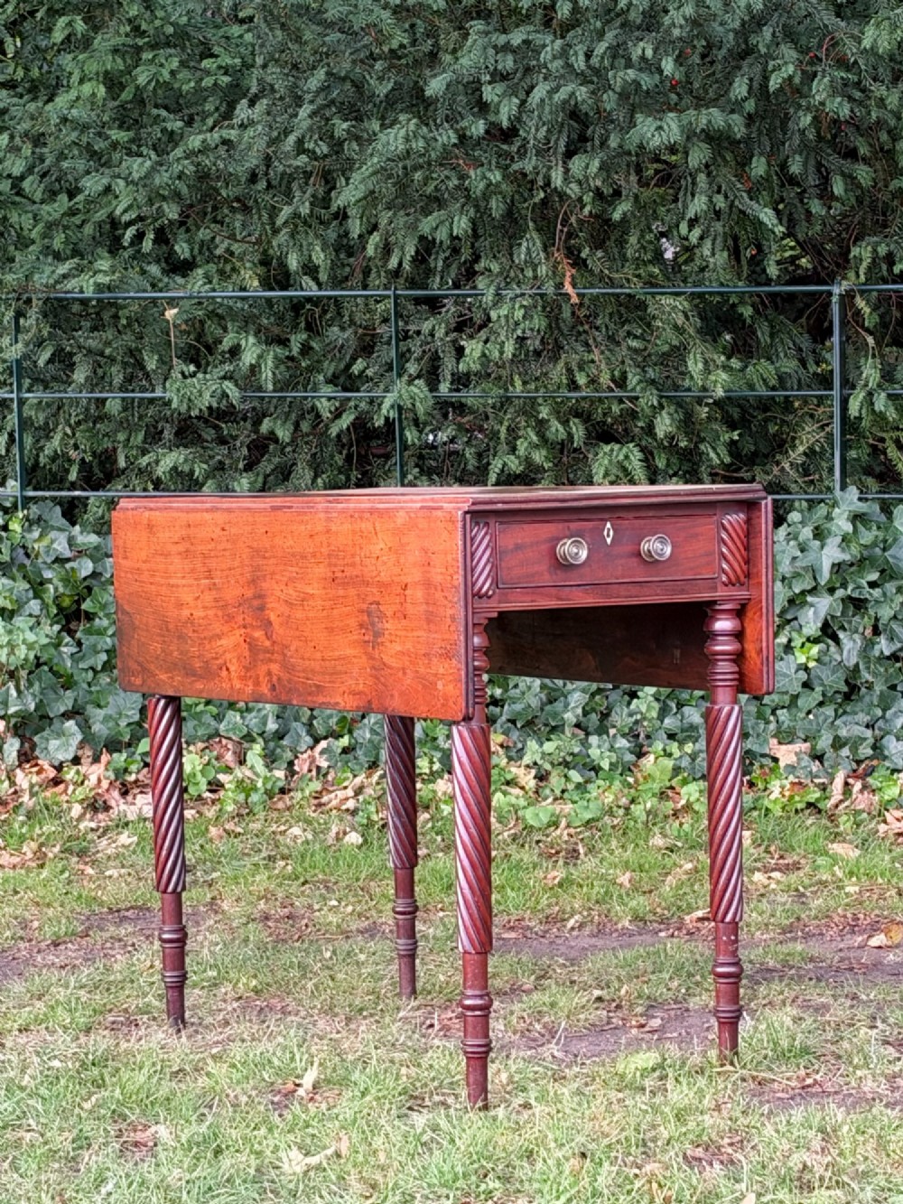 A George IV mahogany drop-leaf table featuring spiral turned legs, a single drawer with twin pull knobs, and two folding side leaves.