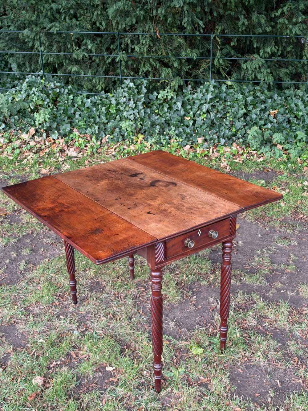 A George IV mahogany drop-leaf table featuring spiral turned legs, a single drawer with twin pull knobs, and two folding side leaves. View IV
