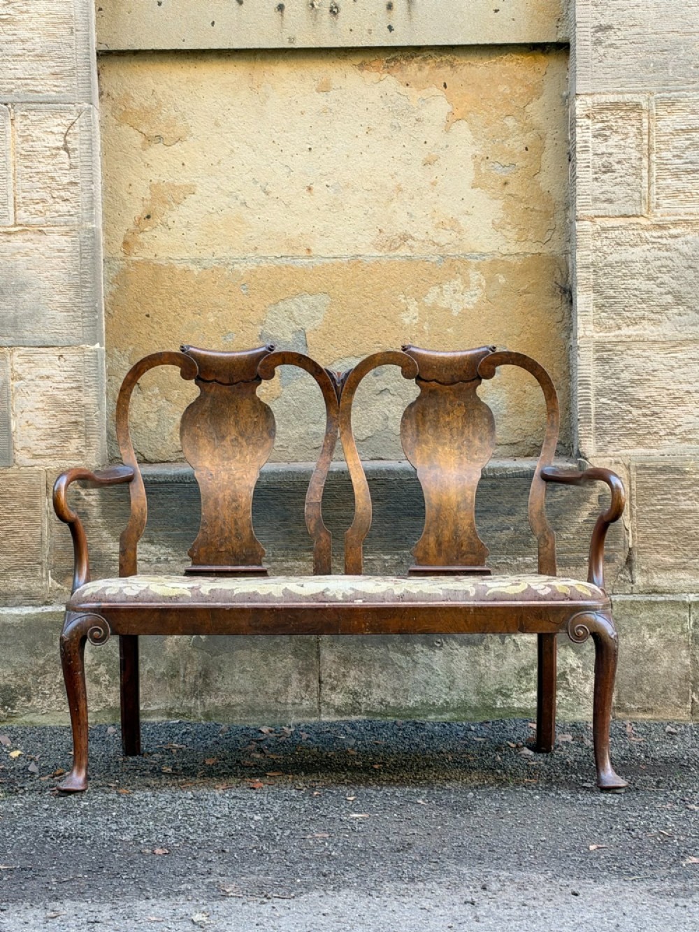 A late nineteenth-century George II style double chair-back settee in warm brown walnut and burr walnut with shepherd crook arms and an upholstered seat.