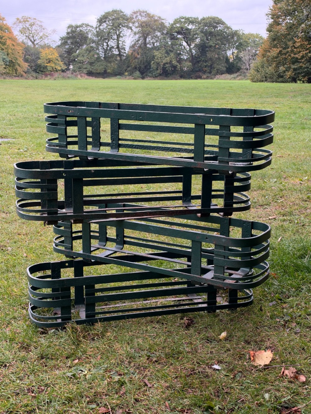 A set of four dark green painted iron strapwork window planters with rounded ends stacked outdoors. View IV