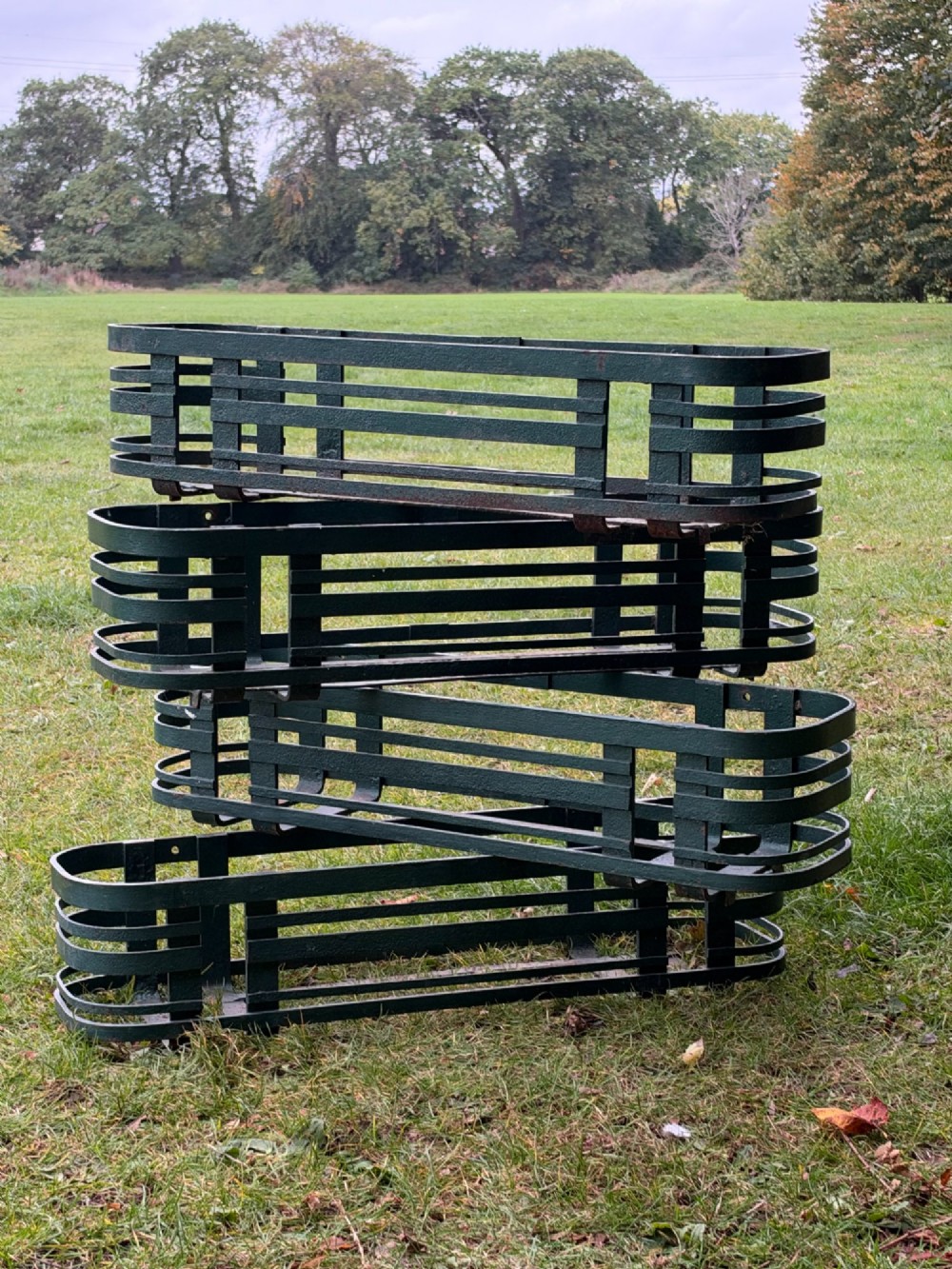 A set of four dark green painted iron strapwork window planters with rounded ends stacked outdoors.