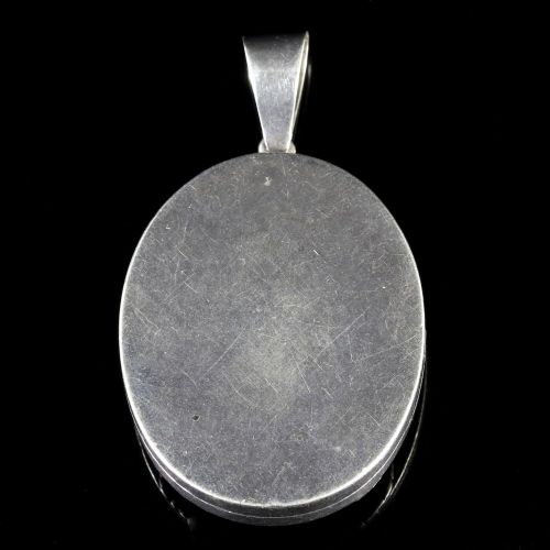 fig 1. An oval Victorian silver locket featuring engraved floral motifs, ropework borders, and a polished suspension bail against a dark background.