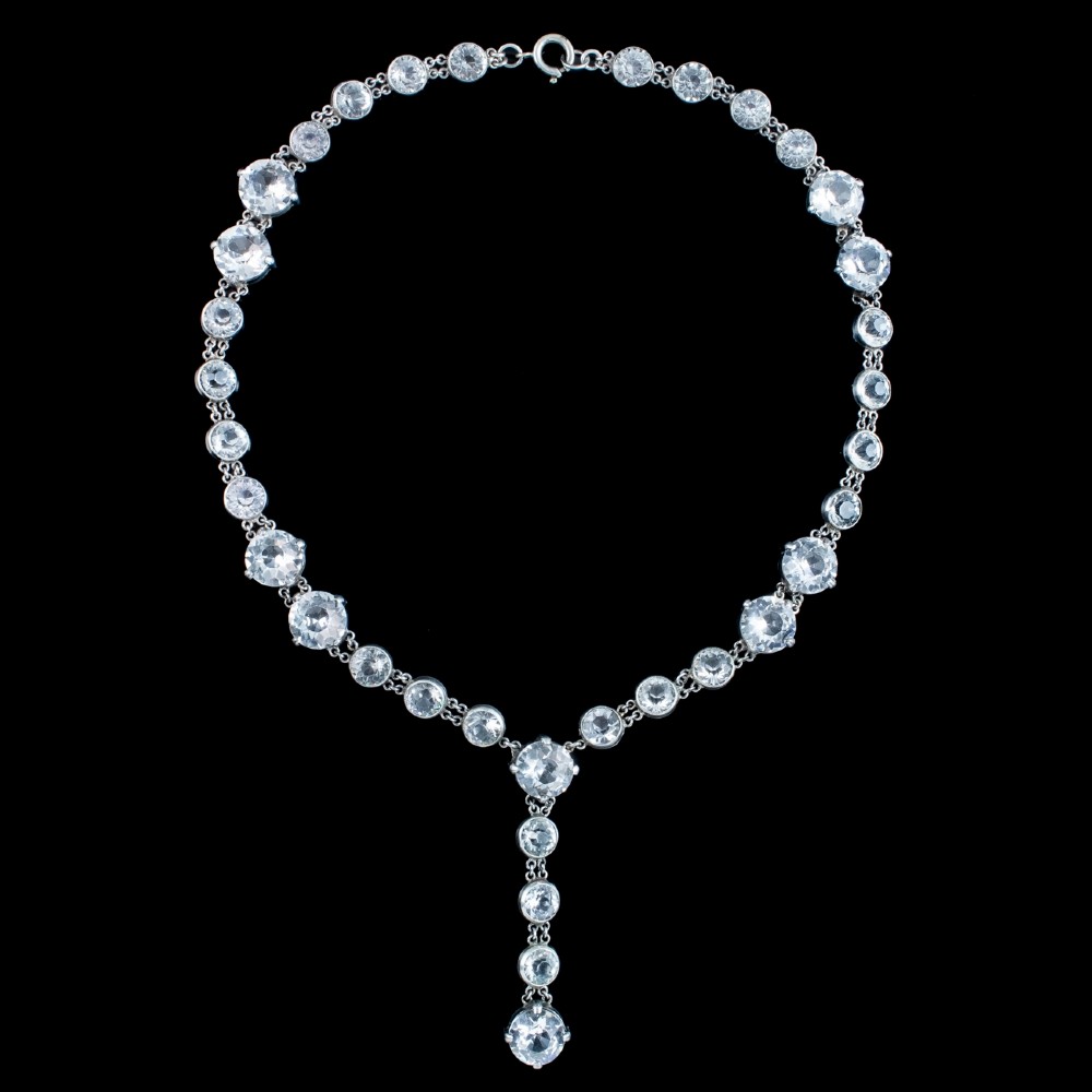 An Art Deco silver necklace featuring a continuous chain of circular clear paste stones with a central linear drop.