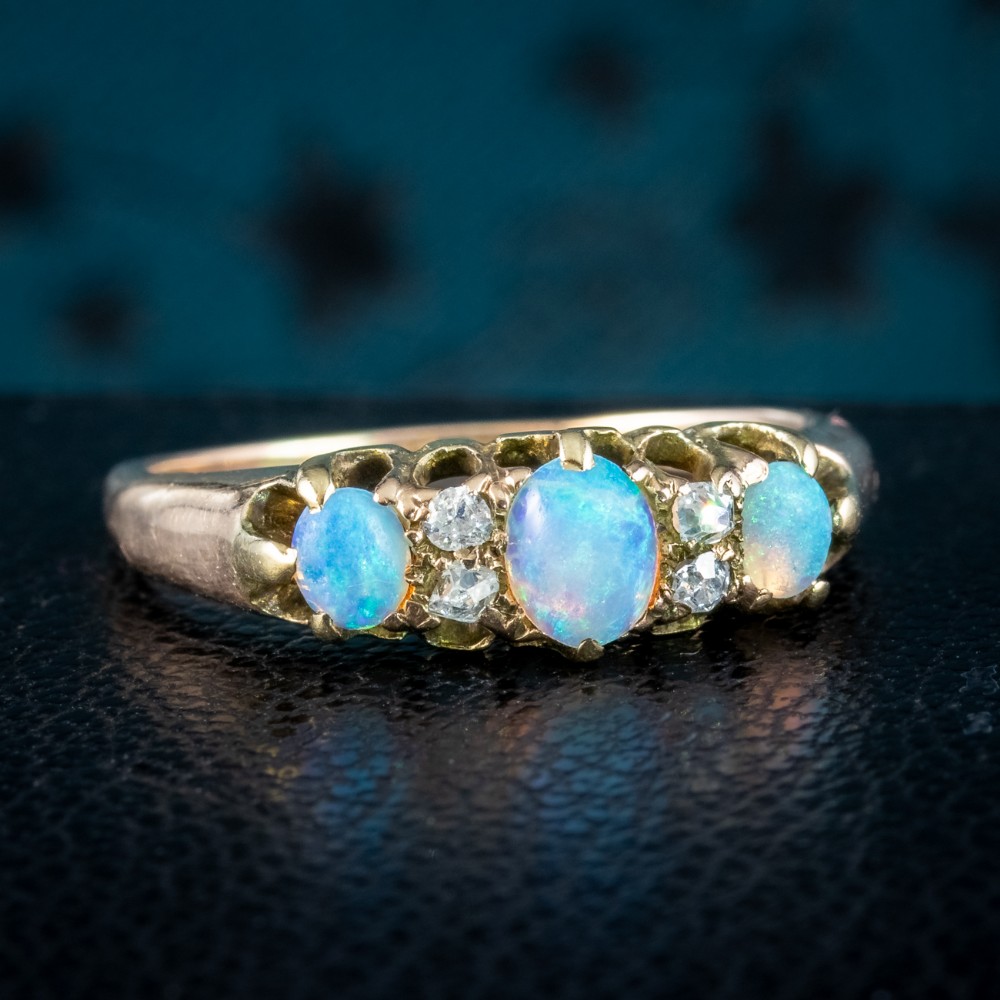 An antique Victorian gold ring set with three oval cabochon opals and four small diamonds in a carved scroll gallery.