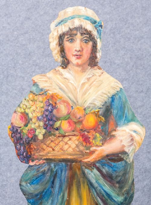 fig 1. A painted wooden dummy board cutout depicting a lady holding a basket filled with fruit, mounted on a rectangular timber base.