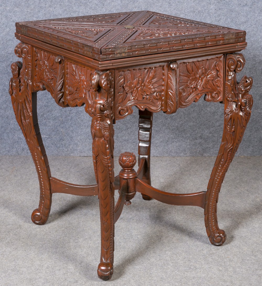 A square carved dark hardwood games table featuring an envelope folding top, intricate dragon carvings, cabriole legs, and an X-frame stretcher.