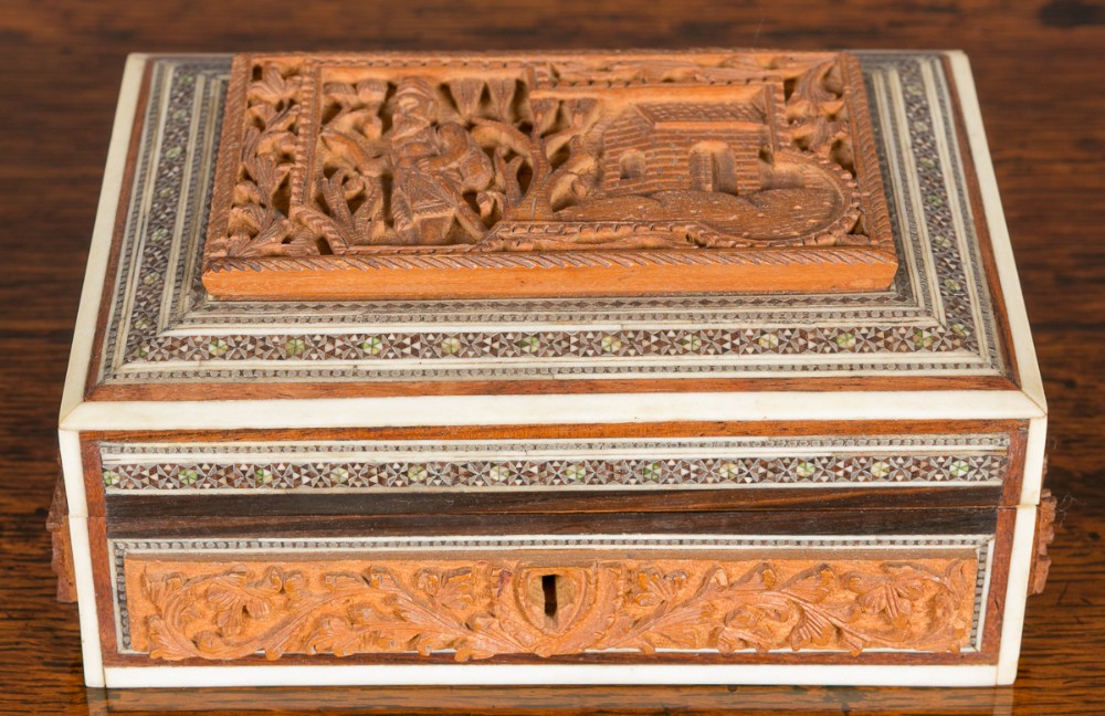 An antique rectangular Anglo-Indian box featuring intricately carved sandalwood panels surrounded by geometric Sadeli micro-mosaic inlay borders.