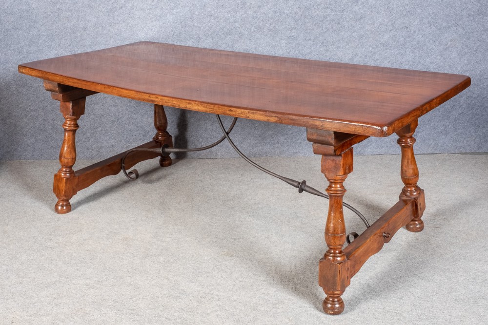 A wooden Spanish style refectory dining table featuring turned baluster legs and curved wrought iron stretchers.