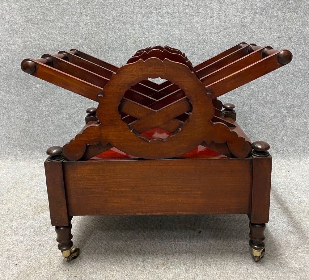An antique mahogany music canterbury featuring carved acanthus side rails, slatted dividers, a single lower drawer with a central knob handle, and turned legs set on brass castors. View VI