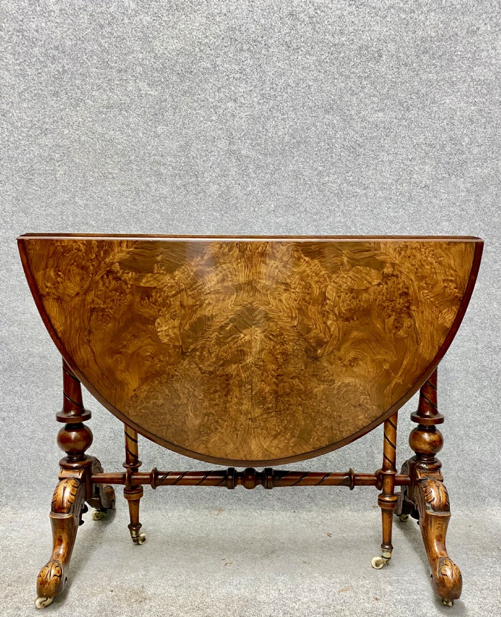 A Victorian burr walnut drop-leaf table featuring symmetrical figured grain, turned supports, spiral stretchers, and carved legs on castors.