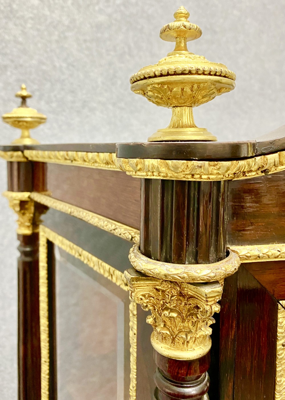 A two-tier dark mahogany display cabinet featuring gilt bronze mounts, glazed panels, fluted columns, and finial decorations. View VII