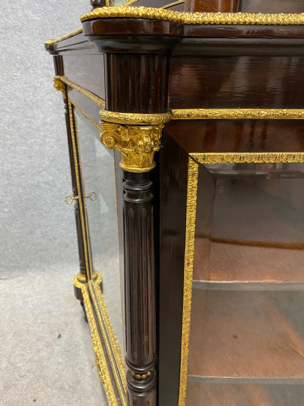 A two-tier dark mahogany display cabinet featuring gilt bronze mounts, glazed panels, fluted columns, and finial decorations. View XI