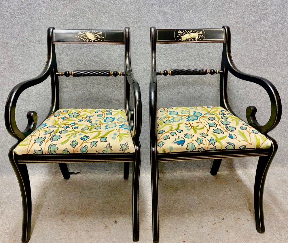 A pair of black ebonised Regency style armchairs featuring gold gilt classical motifs on the top rails, swept scrolled arms, and botanical fabric seats. View II