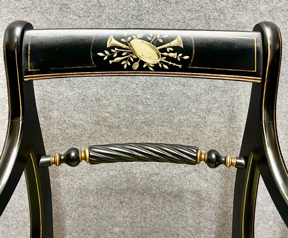 A pair of black ebonised Regency style armchairs featuring gold gilt classical motifs on the top rails, swept scrolled arms, and botanical fabric seats. View V
