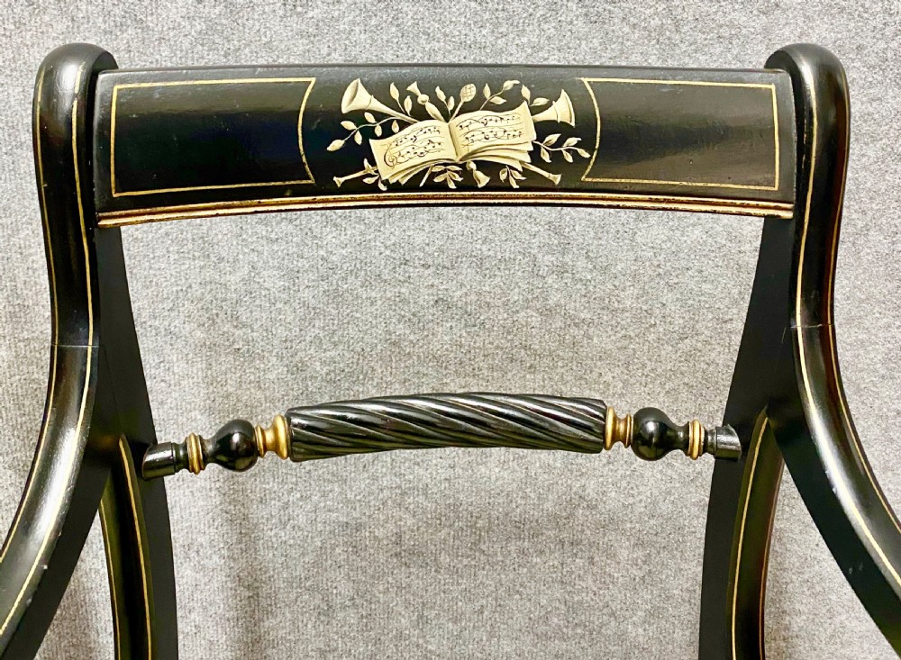 A pair of black ebonised Regency style armchairs featuring gold gilt classical motifs on the top rails, swept scrolled arms, and botanical fabric seats. View VI