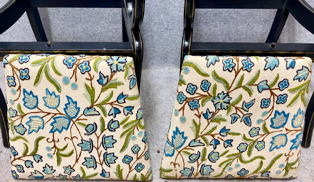 A pair of black ebonised Regency style armchairs featuring gold gilt classical motifs on the top rails, swept scrolled arms, and botanical fabric seats. View VIII