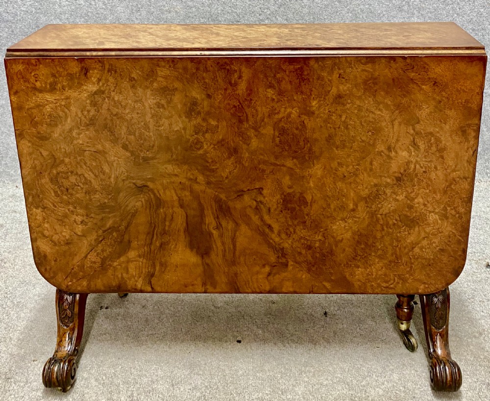 A Victorian burr walnut Sutherland table shown with its drop leaves closed, displaying swirling wood grain veneers, carved legs, and brass castors.