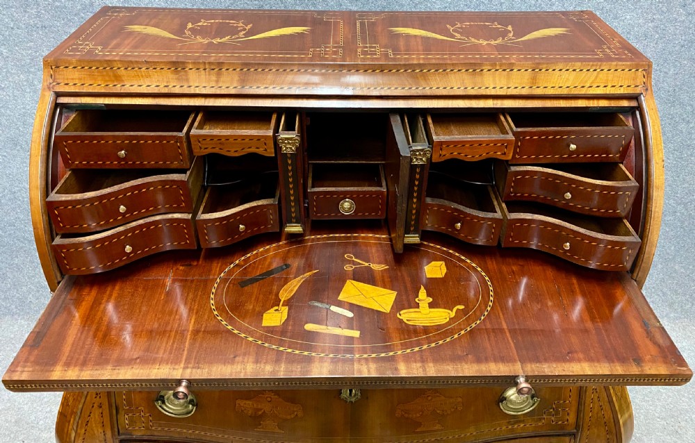 A Dutch marquetry cylinder bureau crafted from warm brown wood with trompe loeil writing tool inlays, fitted drawers, brass handles, and a curved bombe base. View III