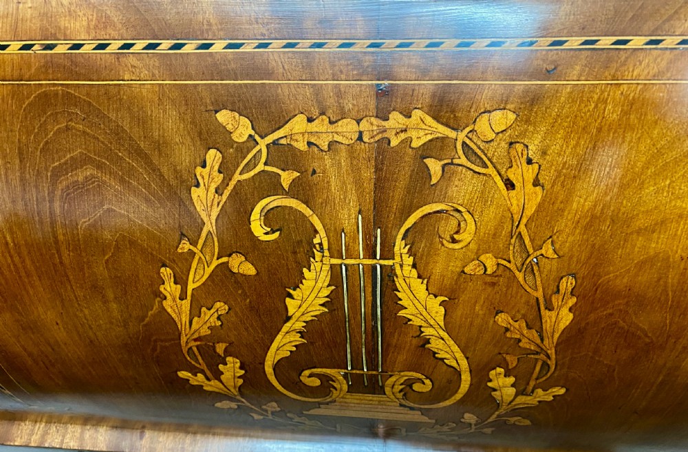 A Dutch marquetry cylinder bureau crafted from warm brown wood with trompe loeil writing tool inlays, fitted drawers, brass handles, and a curved bombe base. View V