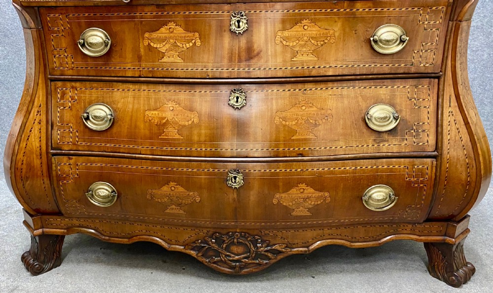 A Dutch marquetry cylinder bureau crafted from warm brown wood with trompe loeil writing tool inlays, fitted drawers, brass handles, and a curved bombe base. View IX