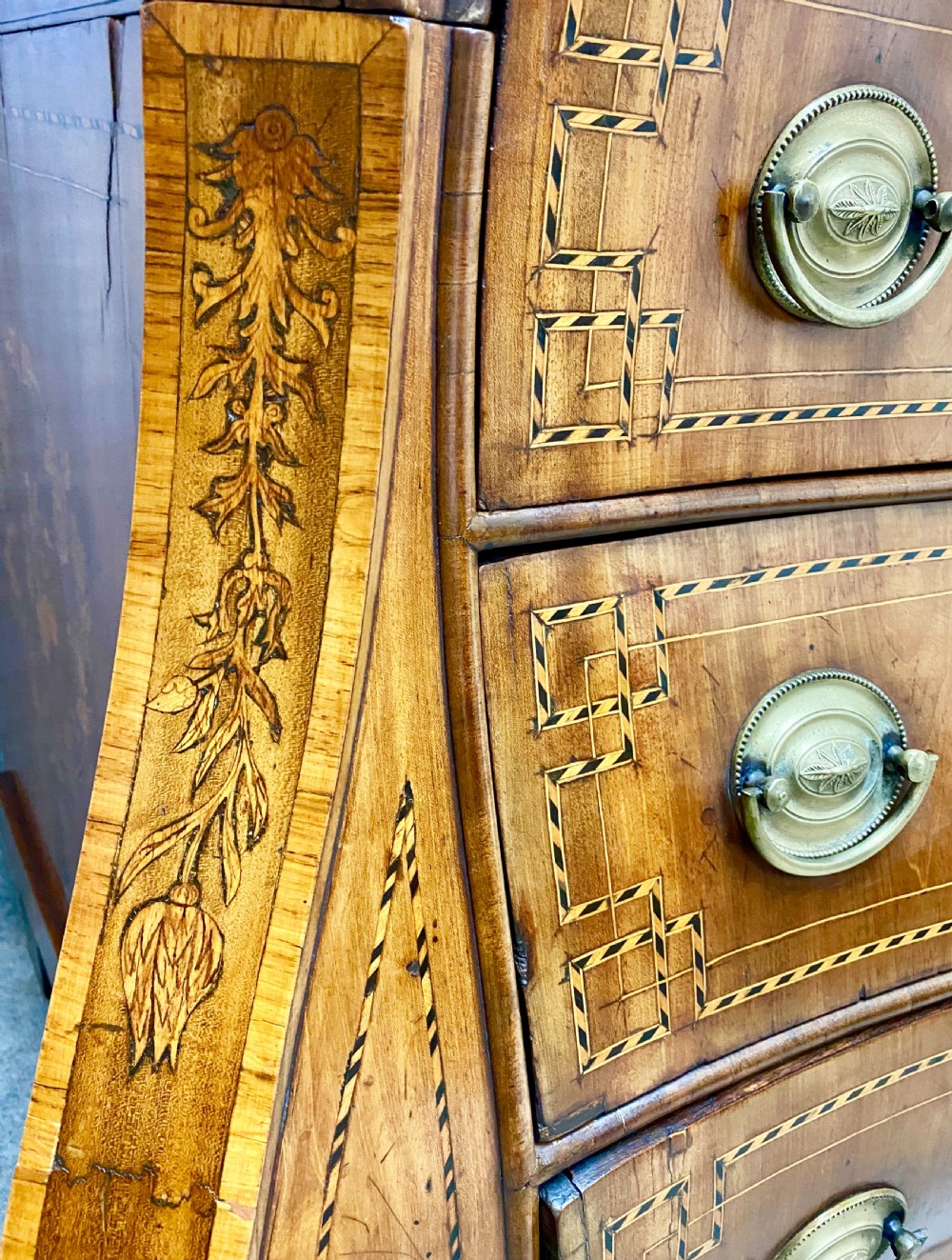 A Dutch marquetry cylinder bureau crafted from warm brown wood with trompe loeil writing tool inlays, fitted drawers, brass handles, and a curved bombe base. View XVI