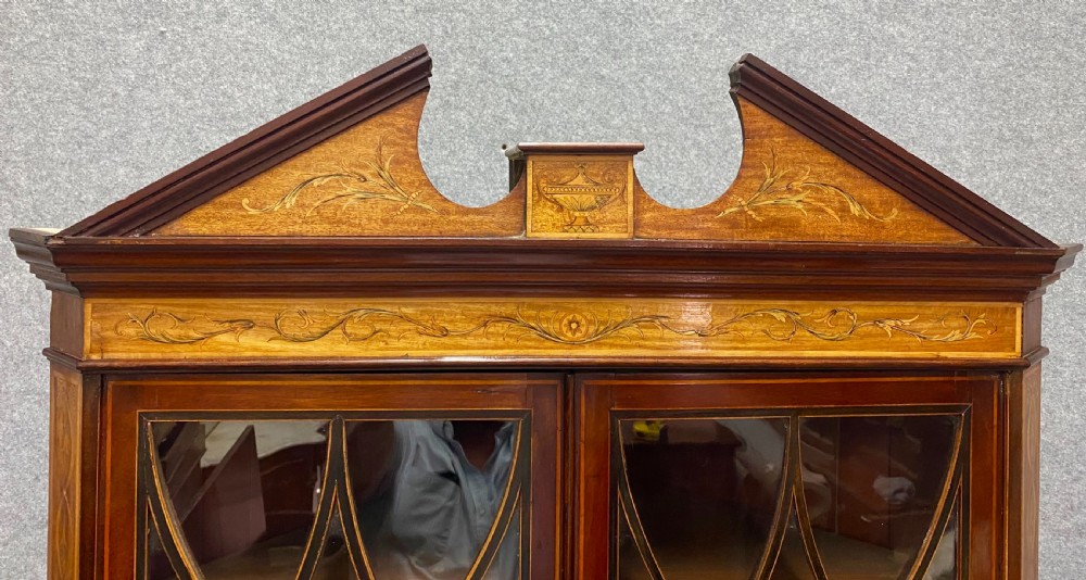 A tall mahogany and satinwood inlaid corner cabinet featuring a broken swan-neck pediment, upper astragal glazed double doors, and lower panelled cupboard doors. View III