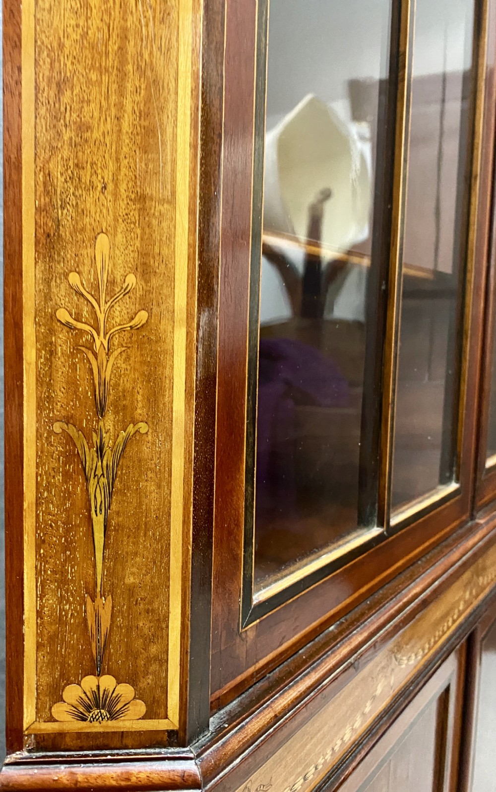 A tall mahogany and satinwood inlaid corner cabinet featuring a broken swan-neck pediment, upper astragal glazed double doors, and lower panelled cupboard doors. View V