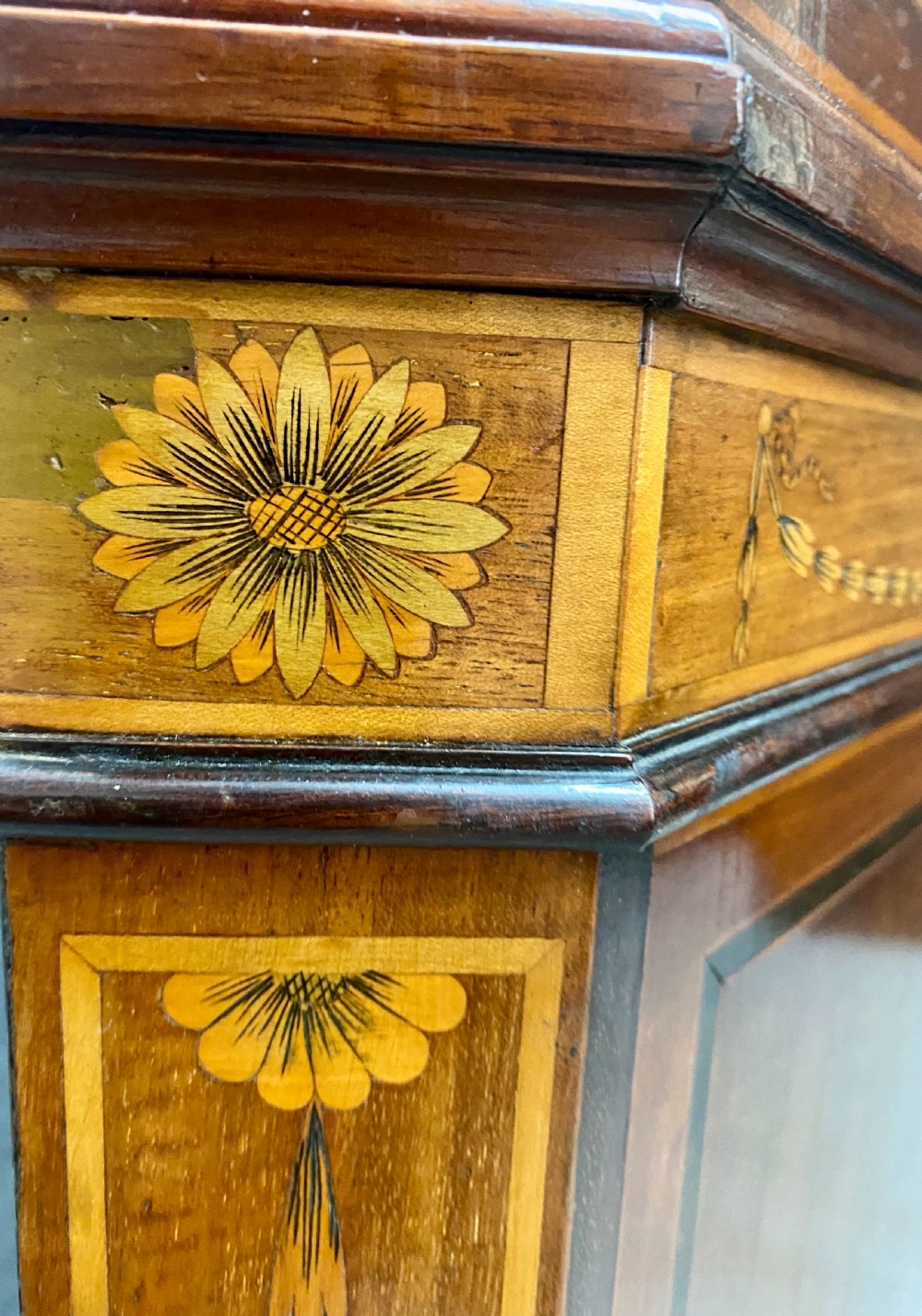 A tall mahogany and satinwood inlaid corner cabinet featuring a broken swan-neck pediment, upper astragal glazed double doors, and lower panelled cupboard doors. View VI