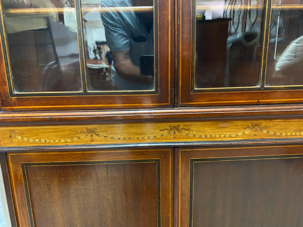 A tall mahogany and satinwood inlaid corner cabinet featuring a broken swan-neck pediment, upper astragal glazed double doors, and lower panelled cupboard doors. View IX
