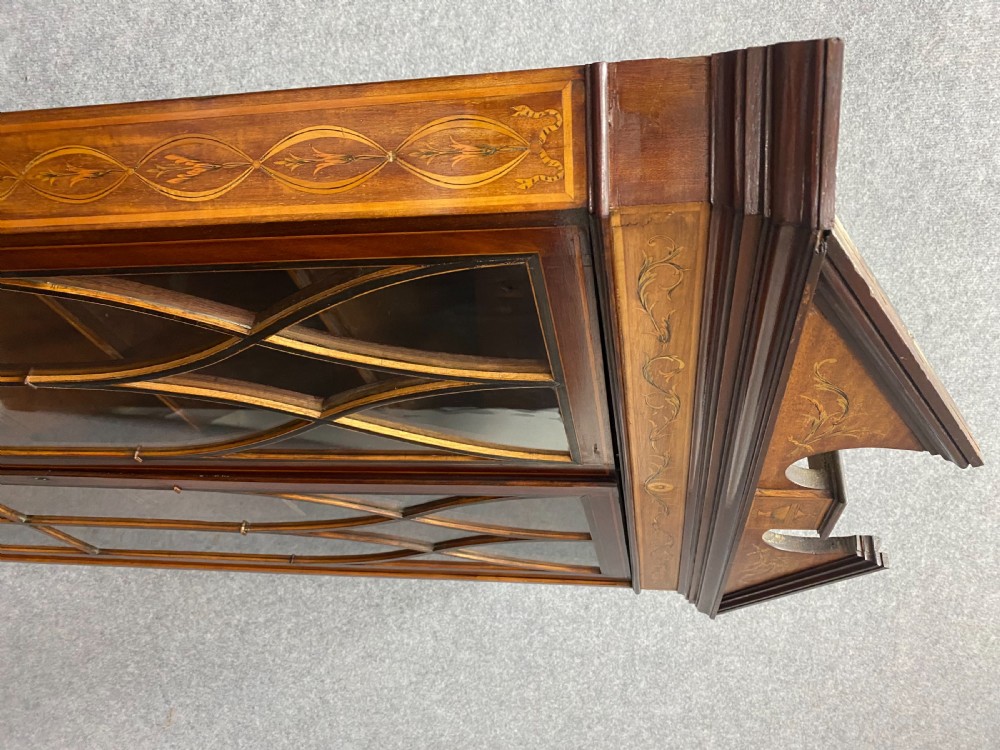 A tall mahogany and satinwood inlaid corner cabinet featuring a broken swan-neck pediment, upper astragal glazed double doors, and lower panelled cupboard doors. View XII