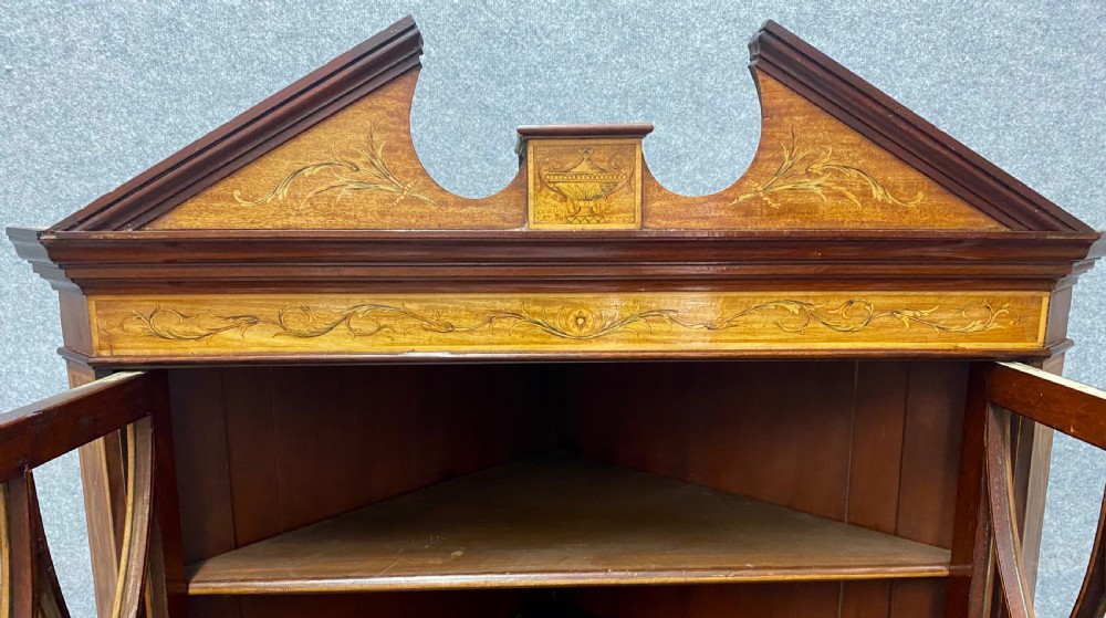 A tall mahogany and satinwood inlaid corner cabinet featuring a broken swan-neck pediment, upper astragal glazed double doors, and lower panelled cupboard doors. View XV