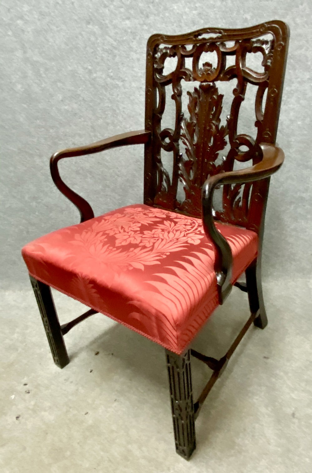 An 18th-century Georgian mahogany elbow chair featuring a detailed pierced splat back, blind fretwork on the front legs, and red patterned damask upholstery.
