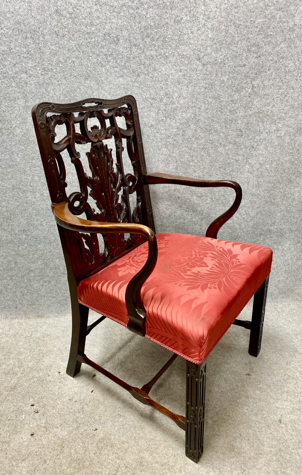 An 18th-century Georgian mahogany elbow chair featuring a detailed pierced splat back, blind fretwork on the front legs, and red patterned damask upholstery. View VI