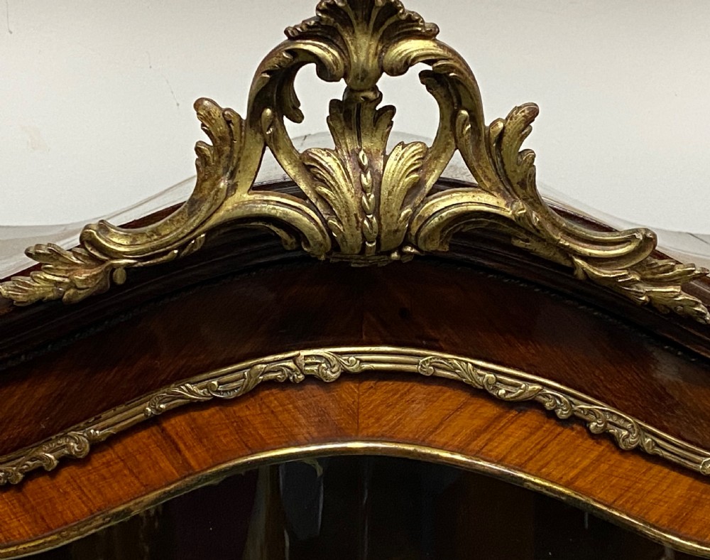 An antique French Louis XV style vitrine featuring serpentine glass sides, ornate gilt bronze mounts, and a lower painted Vernis Martin panel on cabriole legs. View XVI