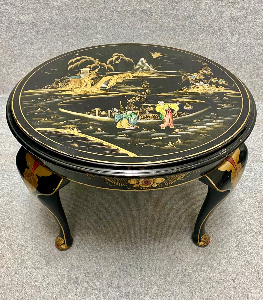 A round black lacquered coffee table with hand-painted gilded Chinoiserie landscape scenes and cabriole legs.
