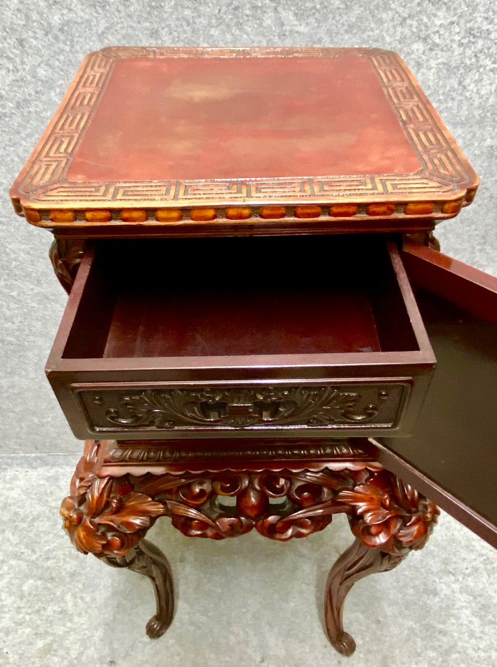 A reddish brown carved cinnabar lacquer cabinet with floral relief panels resting on a tall cabriole leg stand with an open side door. View III