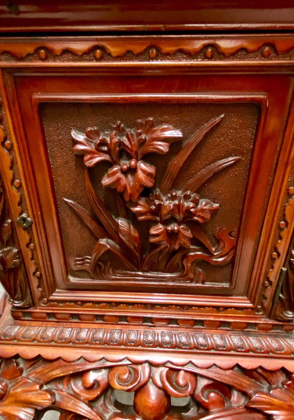 A reddish brown carved cinnabar lacquer cabinet with floral relief panels resting on a tall cabriole leg stand with an open side door. View IV