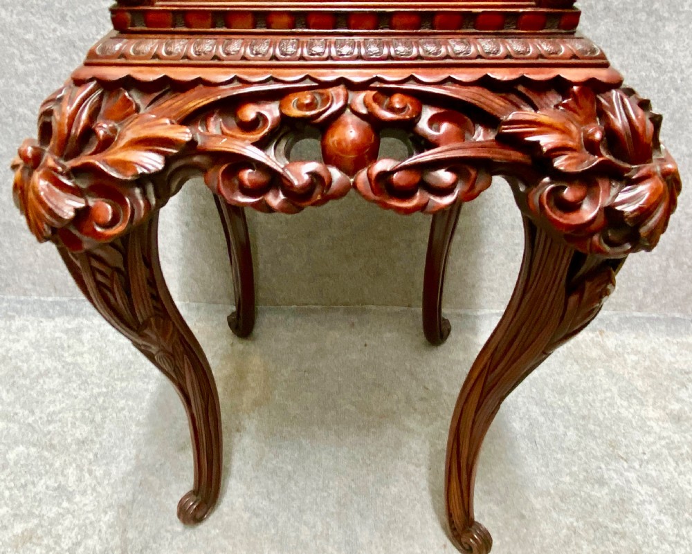 A reddish brown carved cinnabar lacquer cabinet with floral relief panels resting on a tall cabriole leg stand with an open side door. View VI